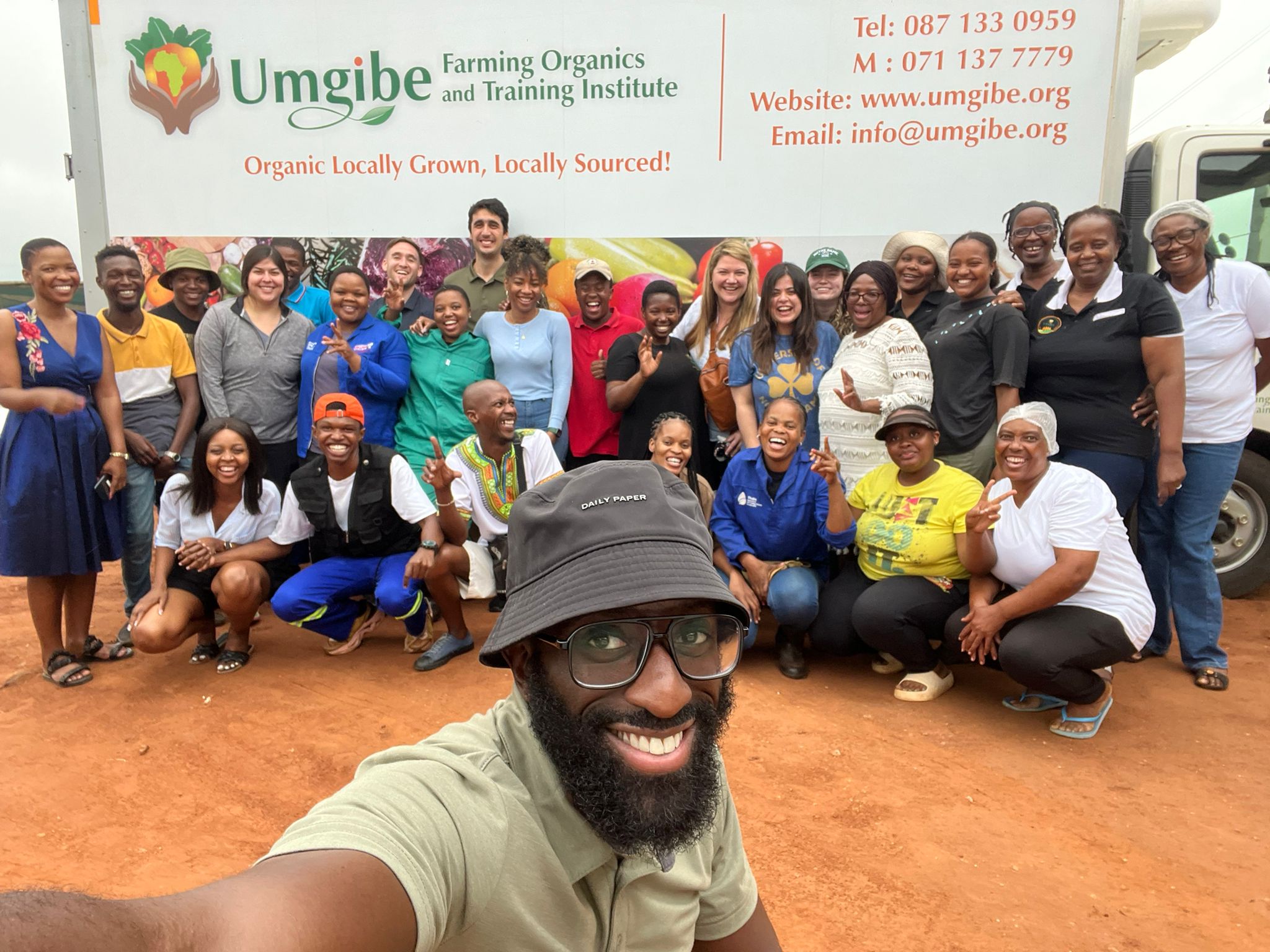 A group of 30 people smile for a group shot together under an Umgibe banner .