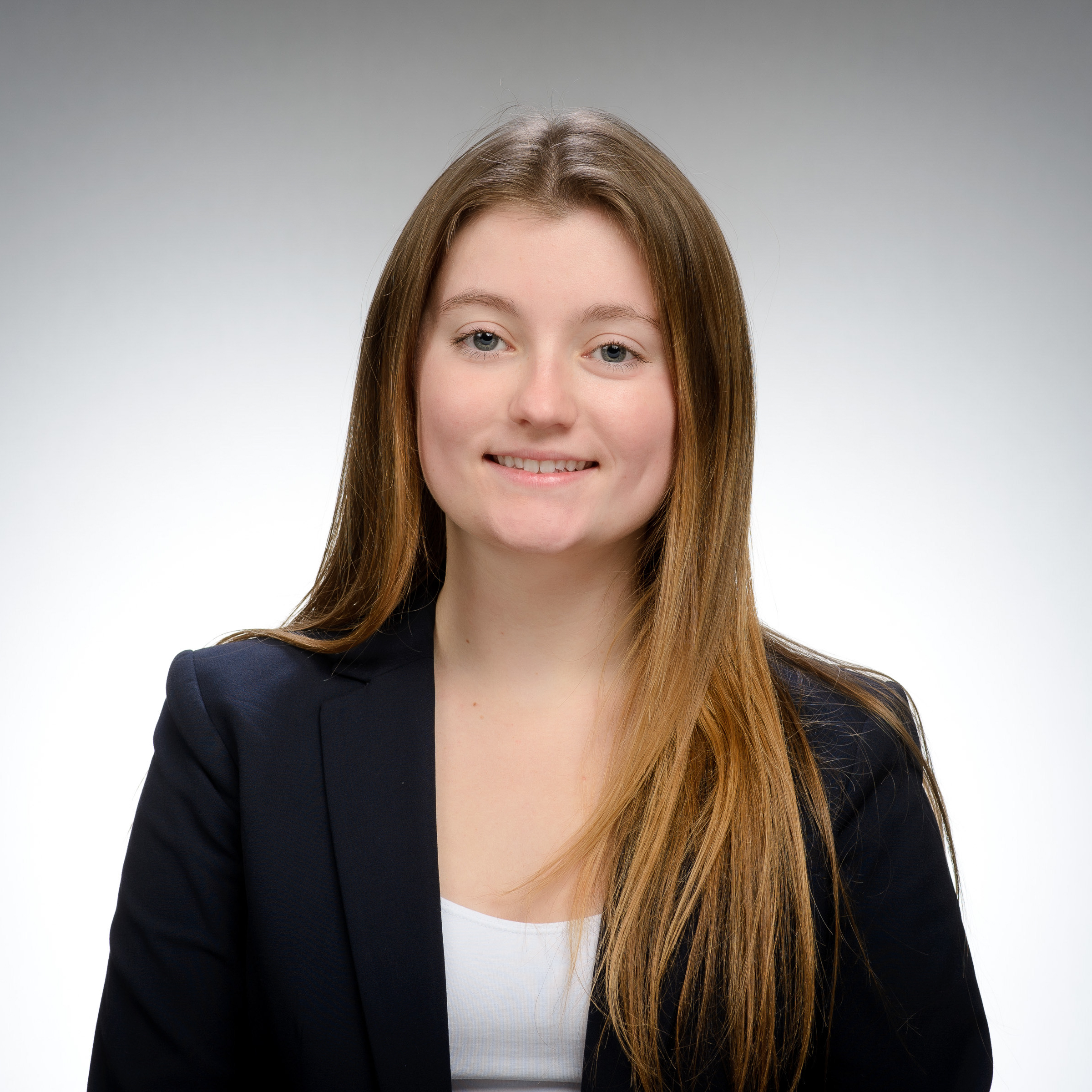 Smiling woman with long hair in a dark blazer and white top, set against a plain studio background.