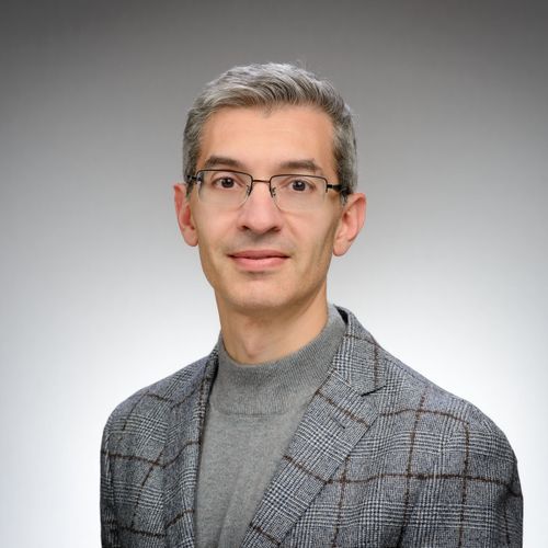 Andrea Tamoni wearing a gray suit in front of gray to white ombre background