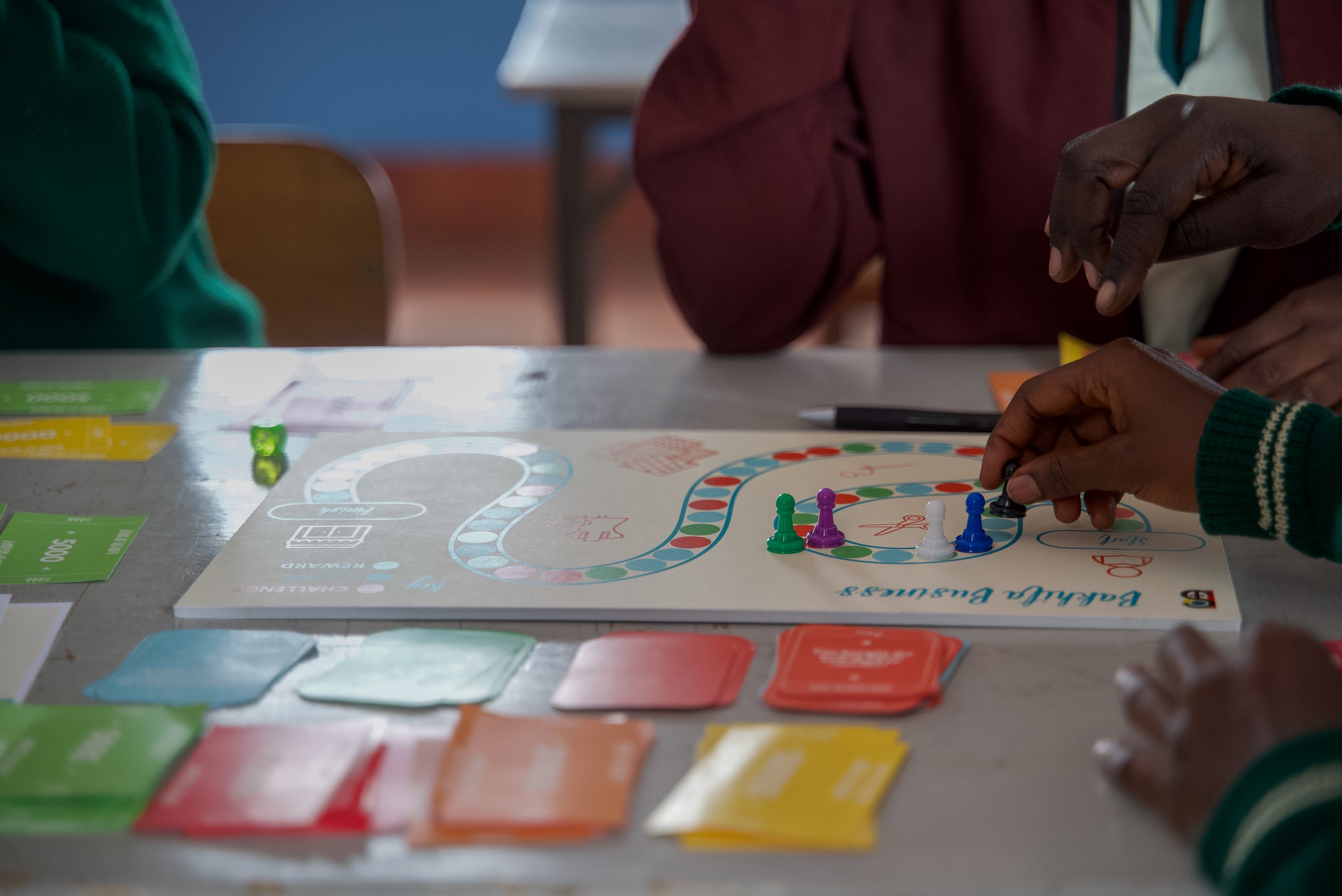 People playing a board game with colorful cards and pieces on a table. Hands are visible moving the pieces.