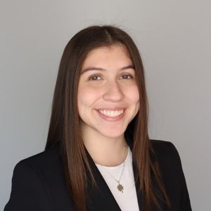 Lindsay Wurth Headshot in front of gray background wearing a black blazer and white shirt