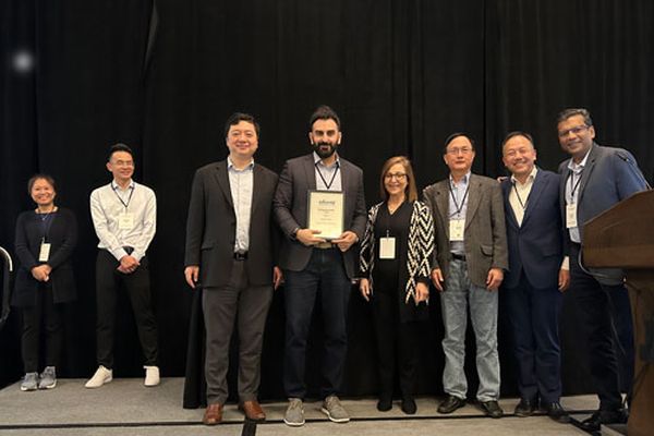 A group of eight people stand on a stage, with one person holding an award plaque. They are dressed in business attire.