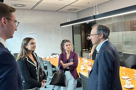 A group of professionals, two women and two men, engage in conversation in a well-lit conference room with a long table.