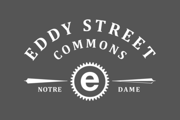 Logo of Eddy Street Commons with "Notre Dame" text, featuring a central gear-like design with the letter "e" all in white text on a grey background.