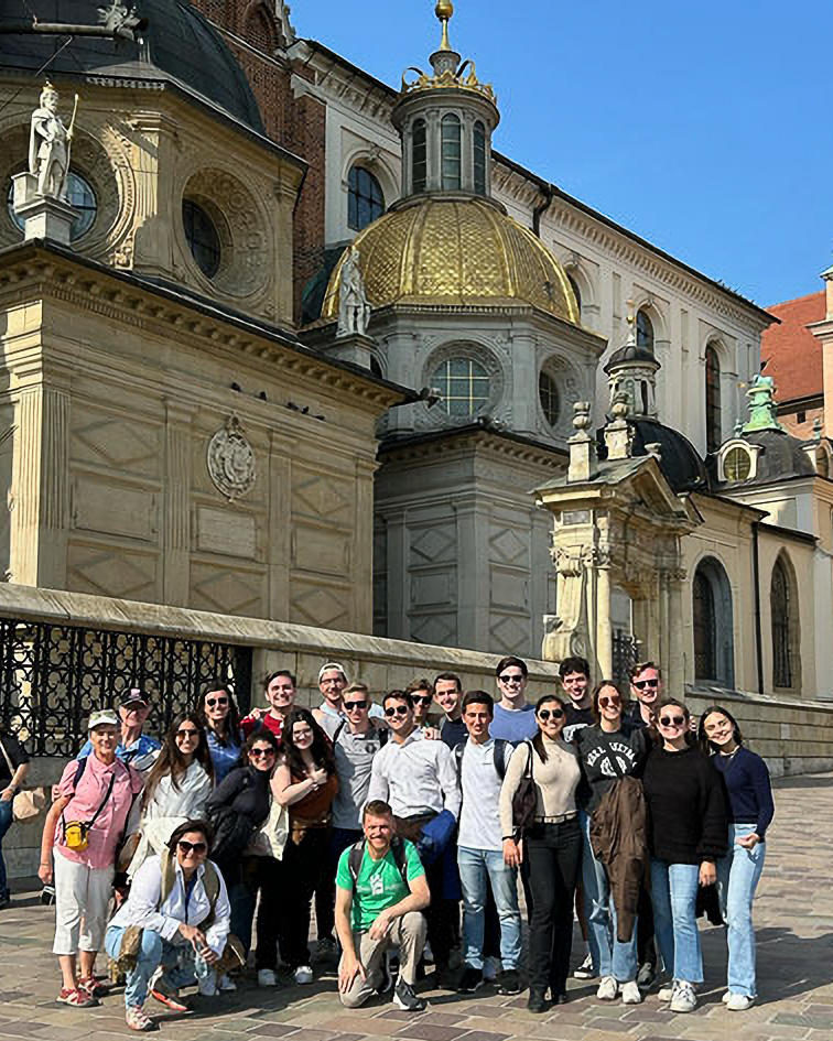 A group of people posing in front of a historic building with ornate domes and intricate carvings, under a clear blue sky.