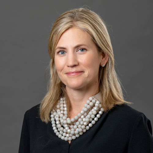 Patty Brady in front of gray background wearing black with white pearl necklace and blonde hair.