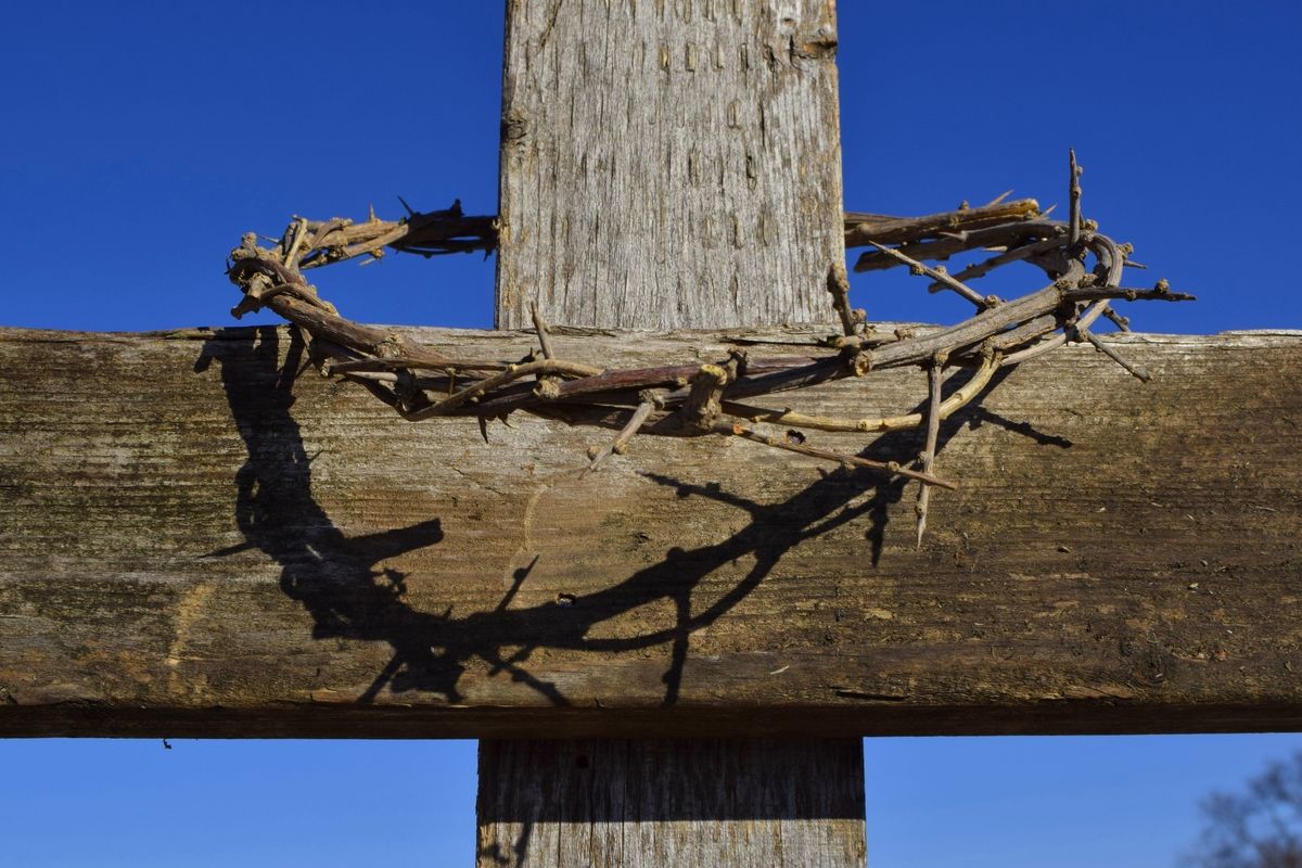 A wooden cross with a crown of thorns casting a shadow against a clear blue sky.