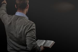 man in gray facing outward holding a bible