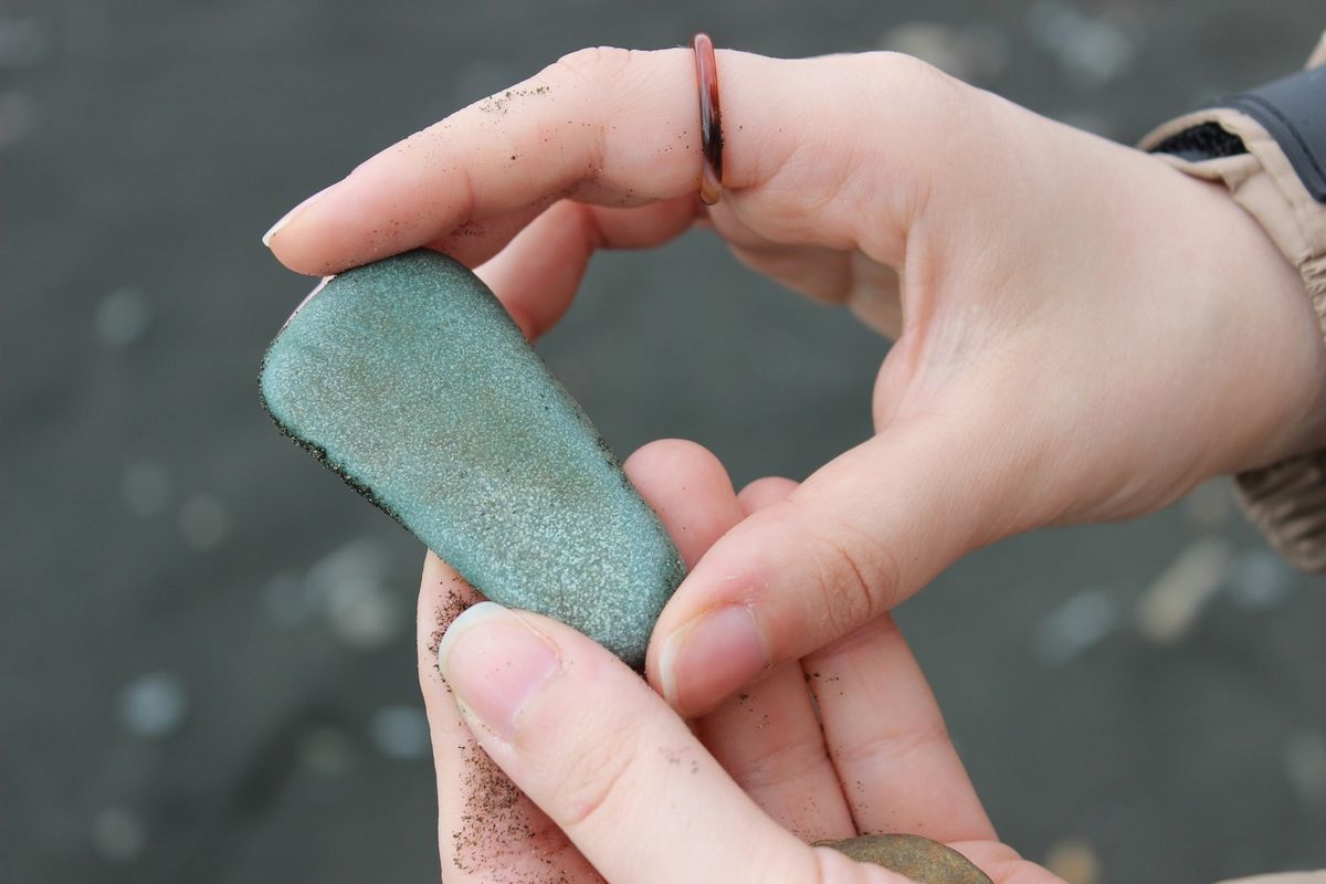 A hand holds a green stone at the seaside.