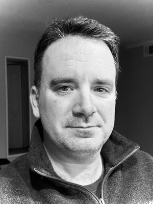 Black and white photo of a white man with short hair wearing a sweater.