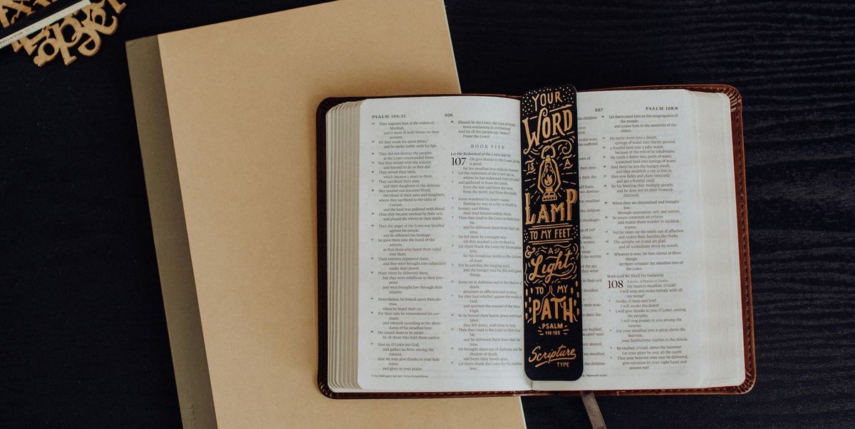 A Bible opened to the book of Psalms lying on top of a notebook with a bookmark reading "Your Word is a Lamp to My Feet" from Psalm 119:105.