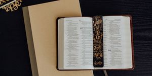 A Bible opened to the book of Psalms lying on top of a notebook with a bookmark reading "Your Word is a Lamp to My Feet" from Psalm 119:105.