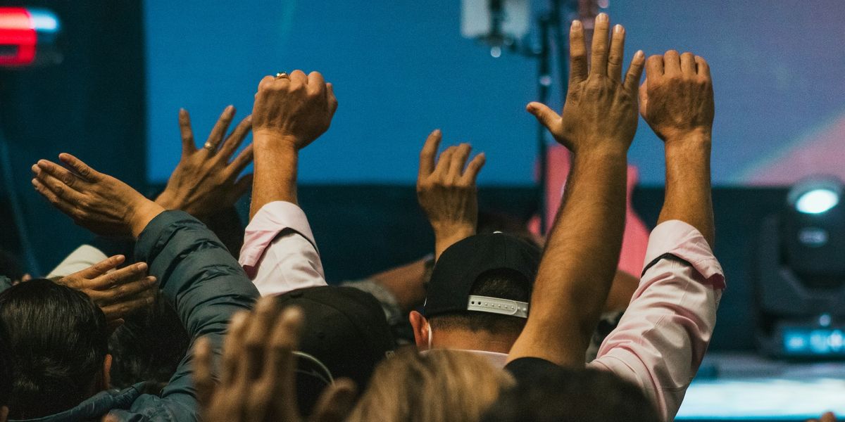 The raised hands of worshippers of different ethnicities.
