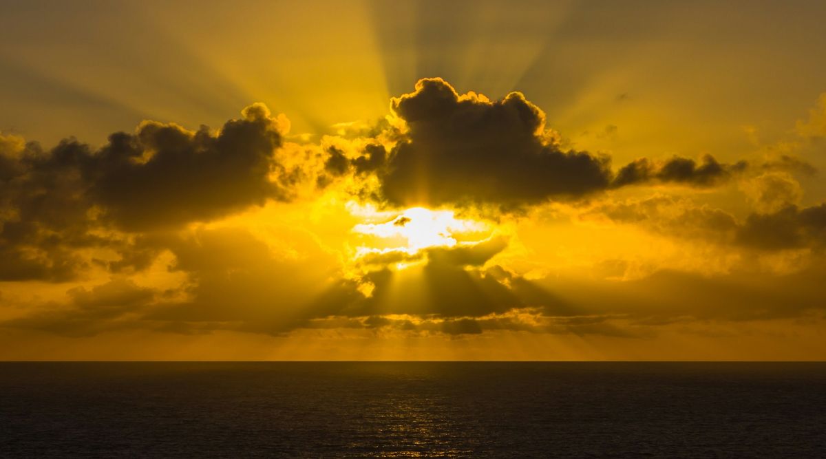 The setting sun shines through clouds over the ocean.