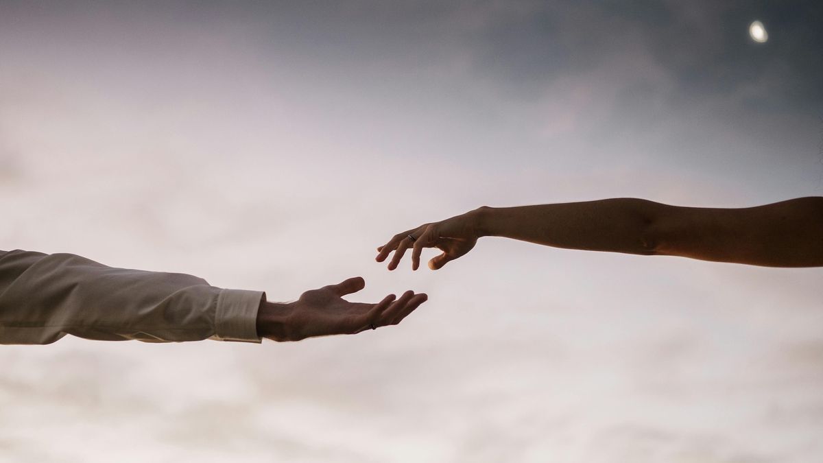 Hands reaching toward each other against a cloudy sky.