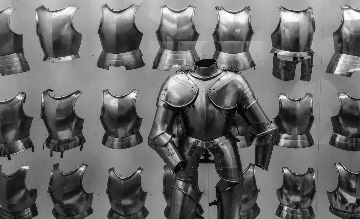 A suit of armor in front of a wall displaying breastplates.