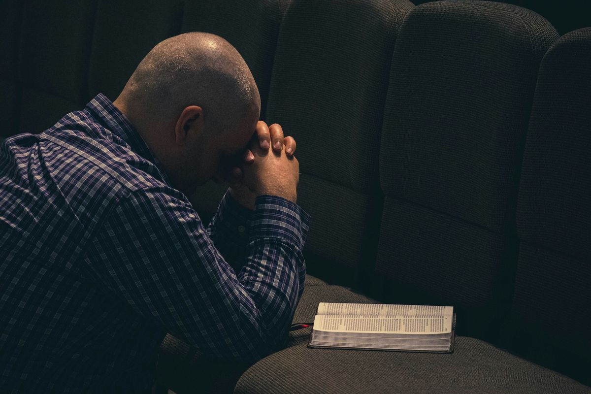 Pastor kneeling in emotional prayer with an open bible.