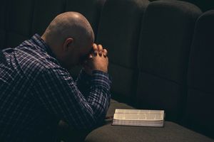 Pastor kneeling in emotional prayer with an open bible.