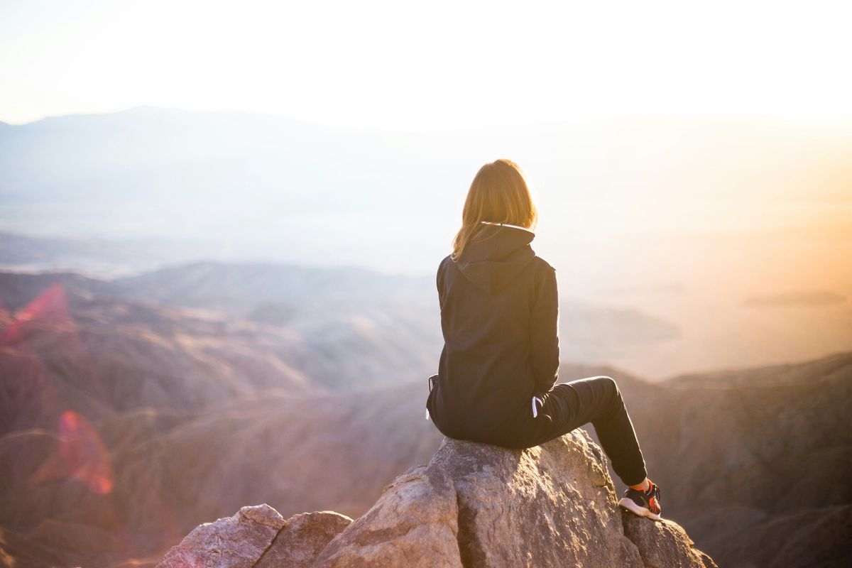 A woman sits on a mountaintop looking across lower hills.