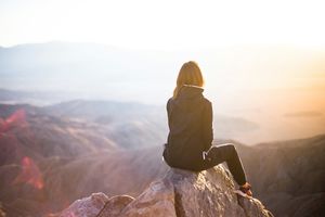 A woman sits on a mountaintop looking across lower hills.