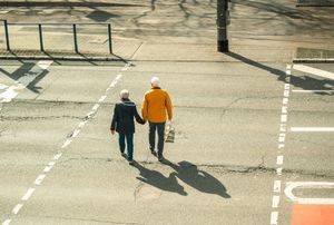 An older couple walks away from the viewer across a street.