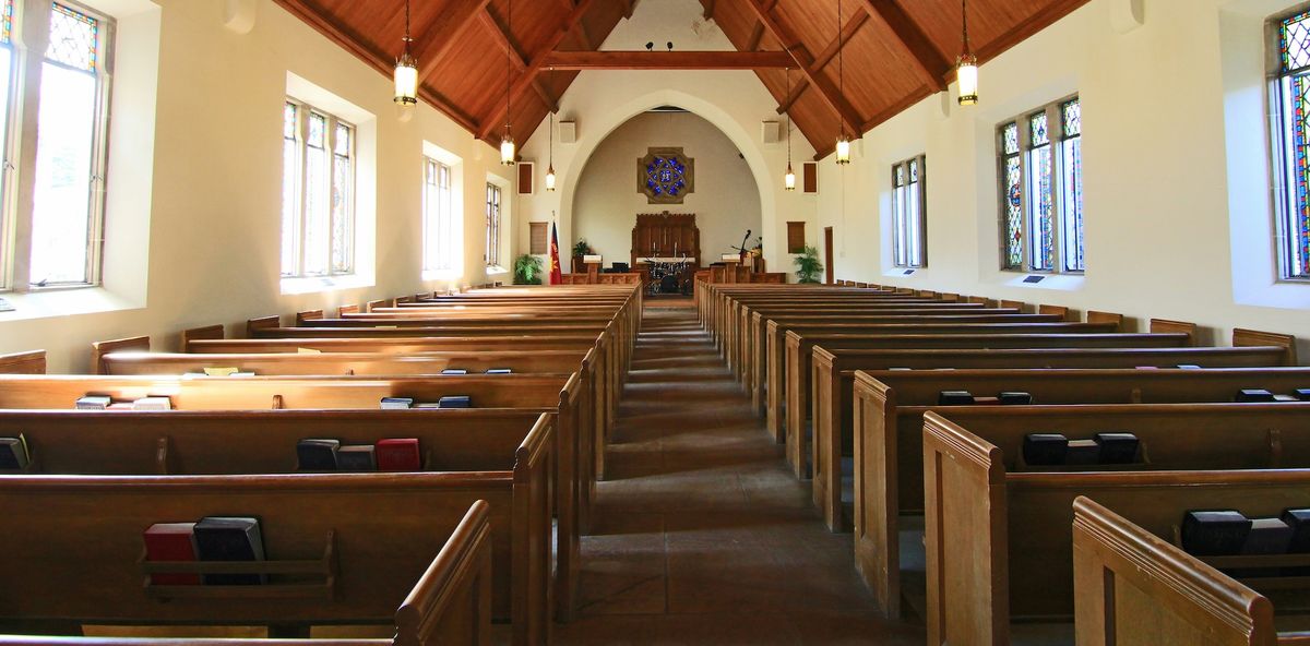 A church sanctuary, with a view down the central aisle toward the altar, with light coming through the windows.