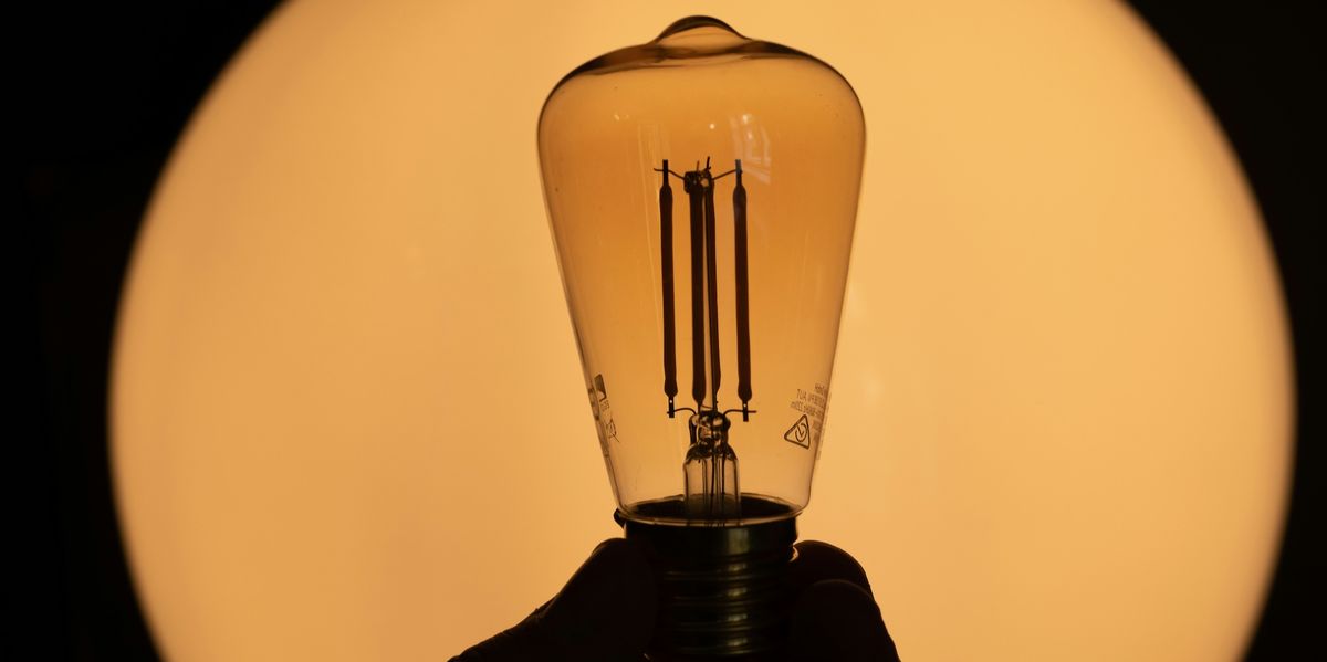 Silhouette of a hand holding a vintage-style light bulb against a warm, glowing background.