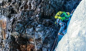 An ice climber clings to a cliff of ice with two ice axes and crampons.