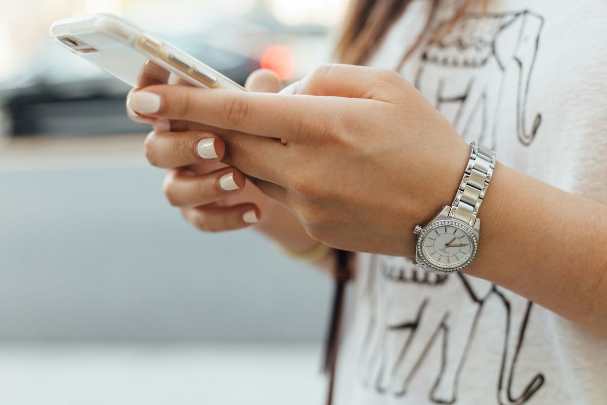Person holding a smartphone, wearing a watch and a shirt with an elephant print.
