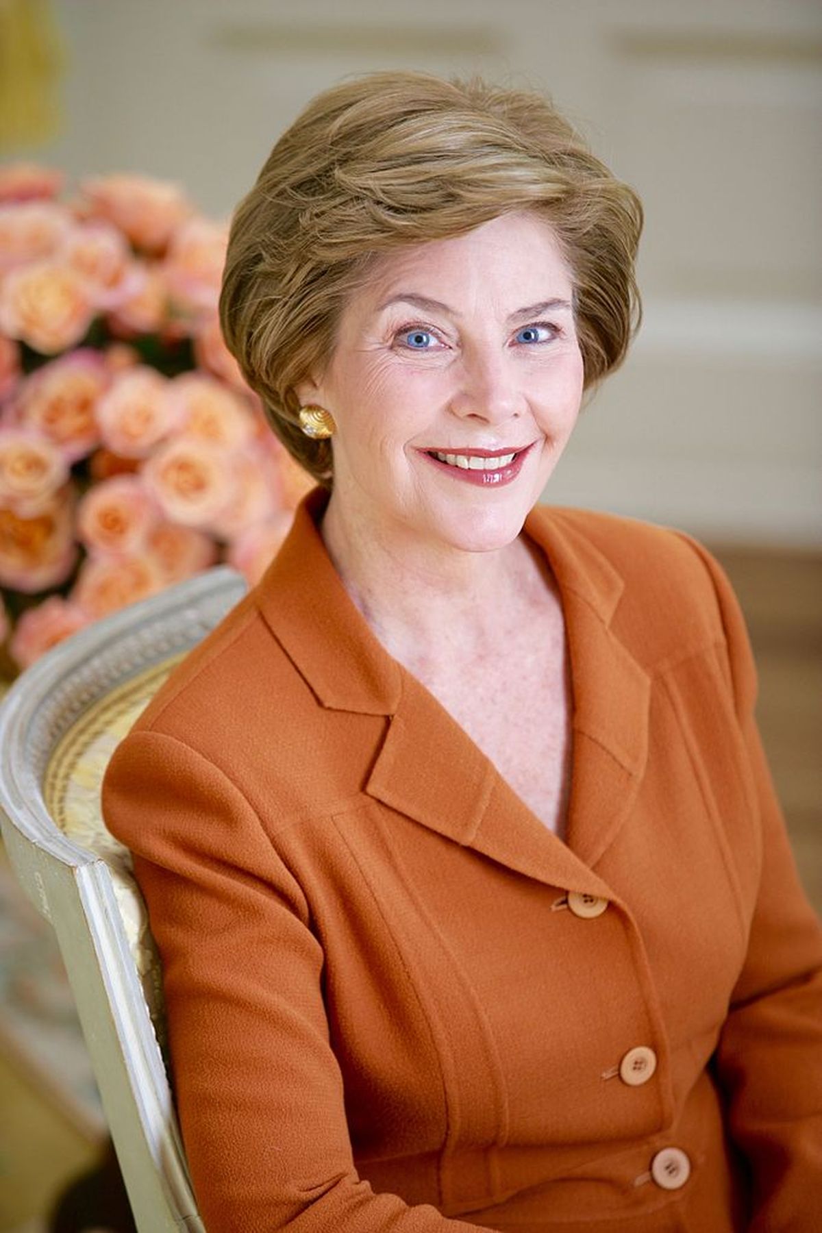 A smiling middle-aged woman with light brown hair and blue eyes looks toward the camera.