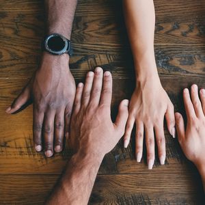 Four hands with different skin tones on a dark brown wood surface.