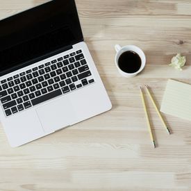 A workspace with a laptop, a cup of coffee, two pencils, an index card, and a balled-up piece of paper.
