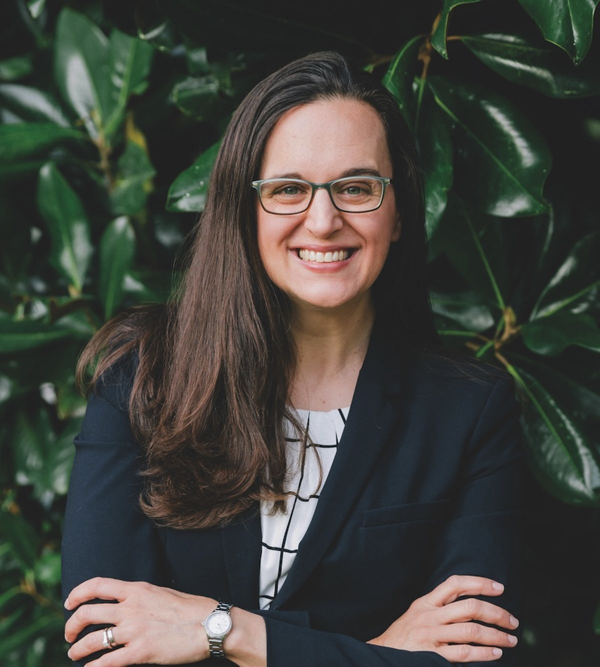 A smiling woman with light skin, glasses, and long, dark hair.