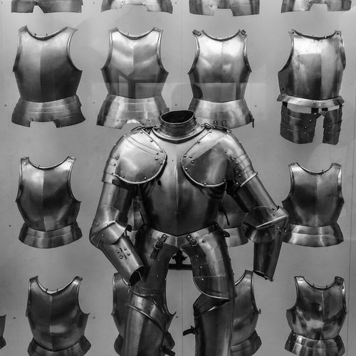 A suit of armor in front of a display of steel breastplates.