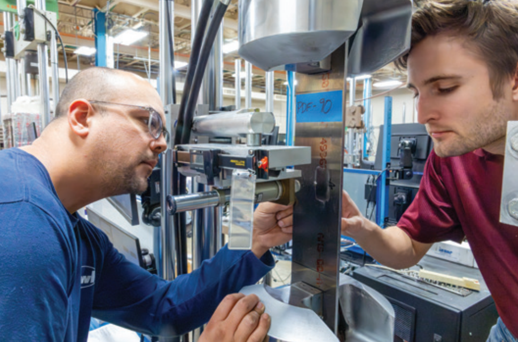 Two workers closely examine a machine in a factory setting, focusing on its details.
