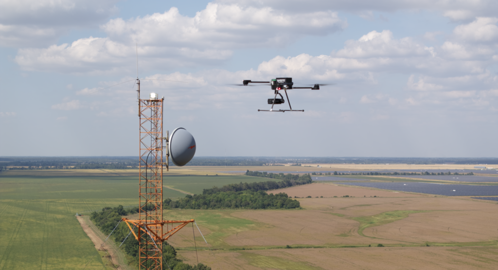 WISPR Scout 2 drone hovering near a communications tower above green farmland during an aerial infrastructure inspection