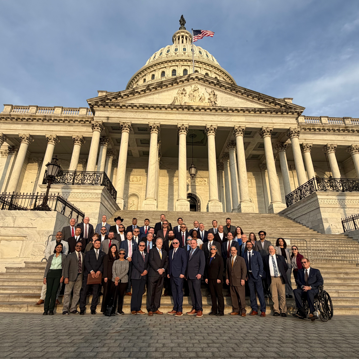 A group of people in formal attire stands on the steps of the United States Capitol.