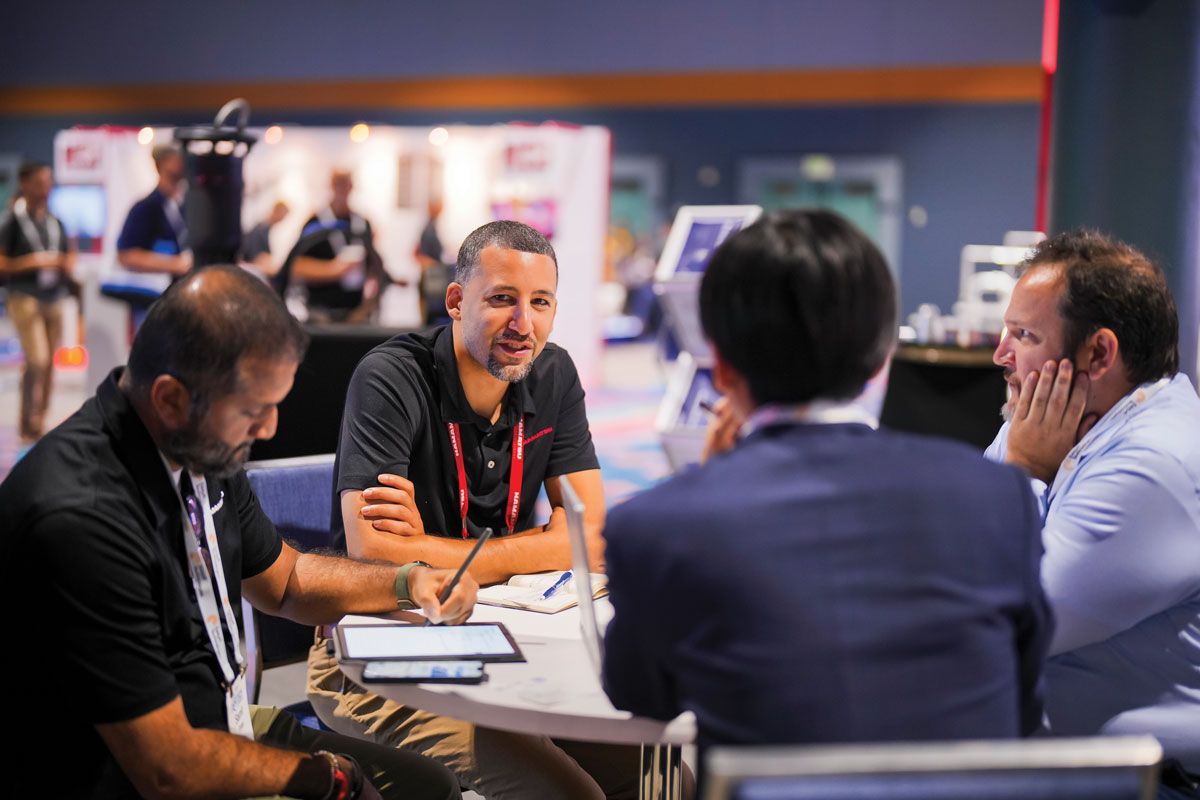 Photograph of attendees networking around a table in the exhibit hall at a past ASNT conference.