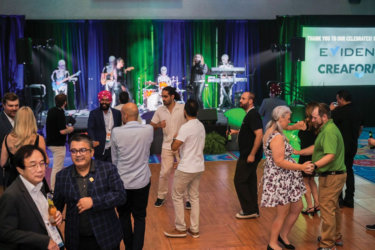 Photograph of attendees mingling at a past ASNT Celebrates! evening reception, with a live band performing on a green-lit stage in the background.