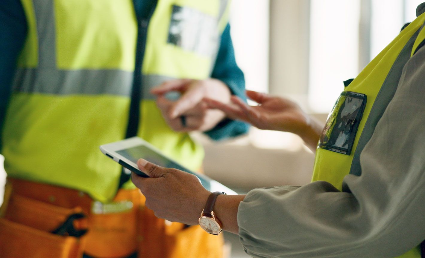 Two workers in high-visibility safety vests reviewing information together on a tablet