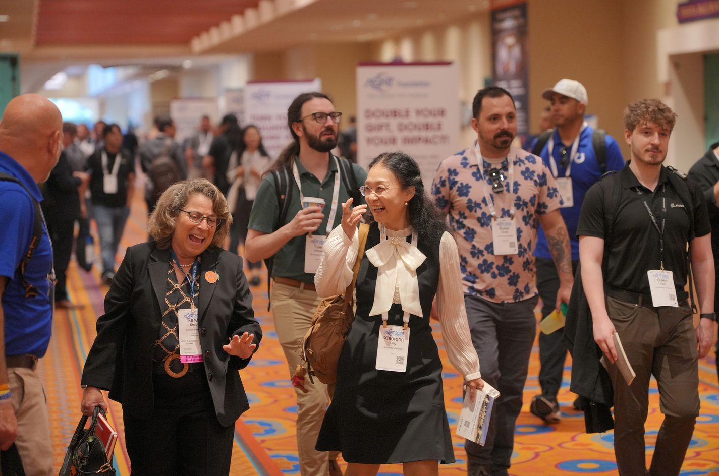 A group of attendees at an ASNT Annual event, walking through the entrance with banners and sponsor logos visible in the background.