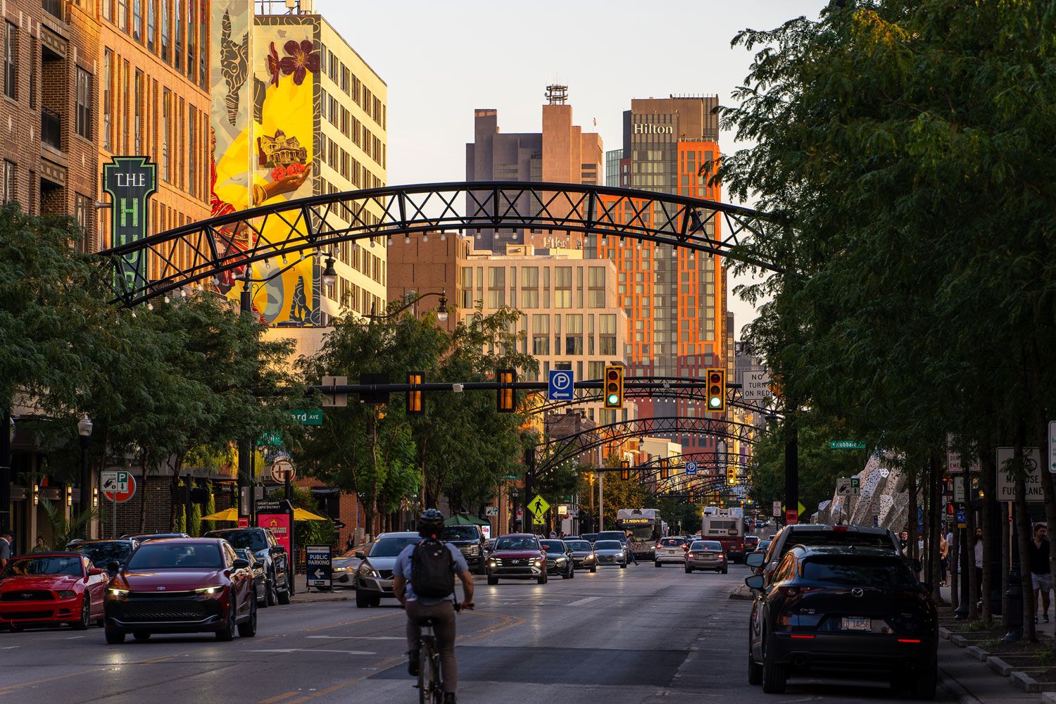 Photograph of the Short North Arts District in Columbus, where a series of lighted metal arches spans High Street above traffic and pedestrians, with downtown buildings beyond.