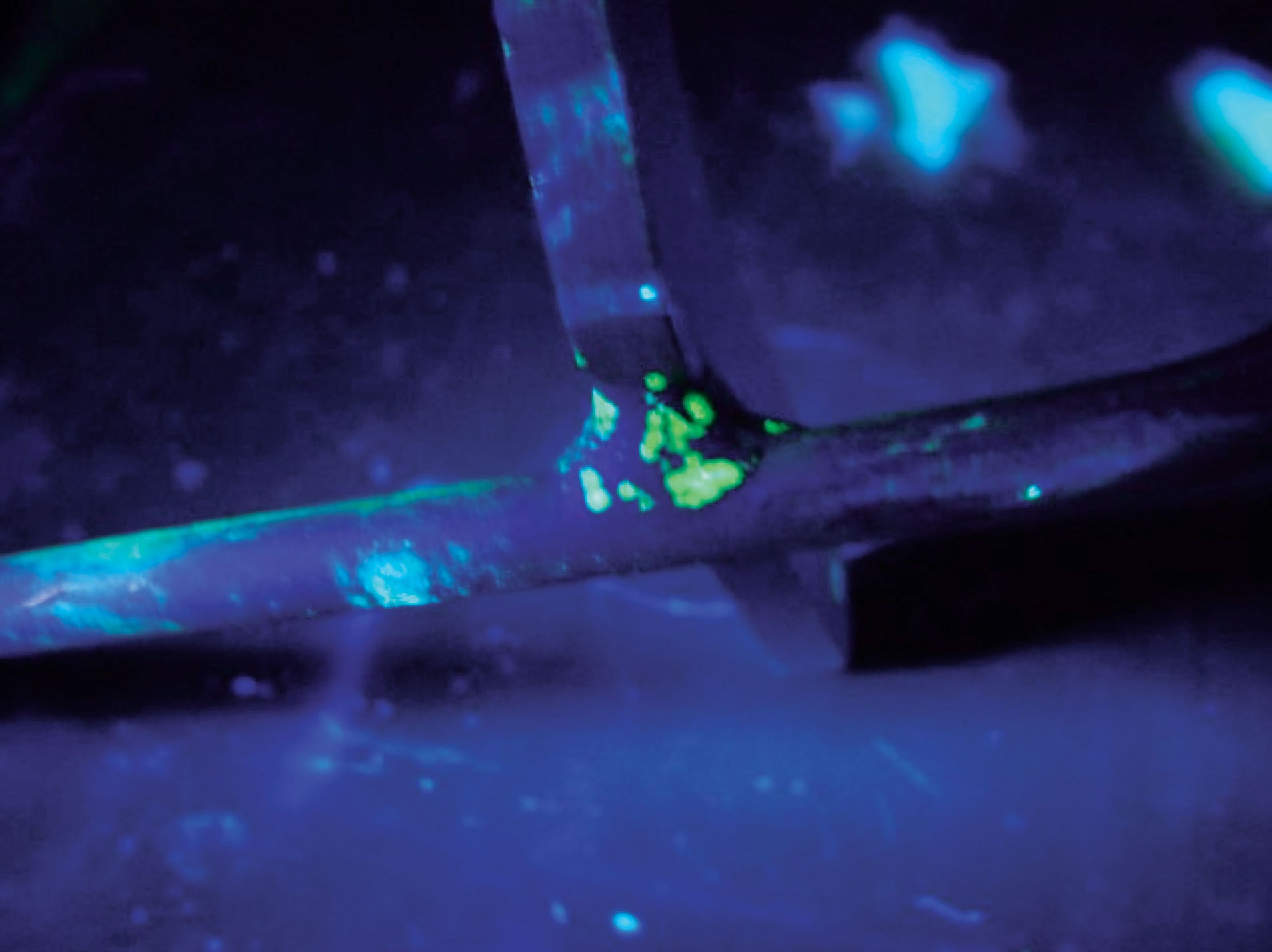 Yellow-green fluorescent penetrant indications glowing on a metal part under UV-A radiation.