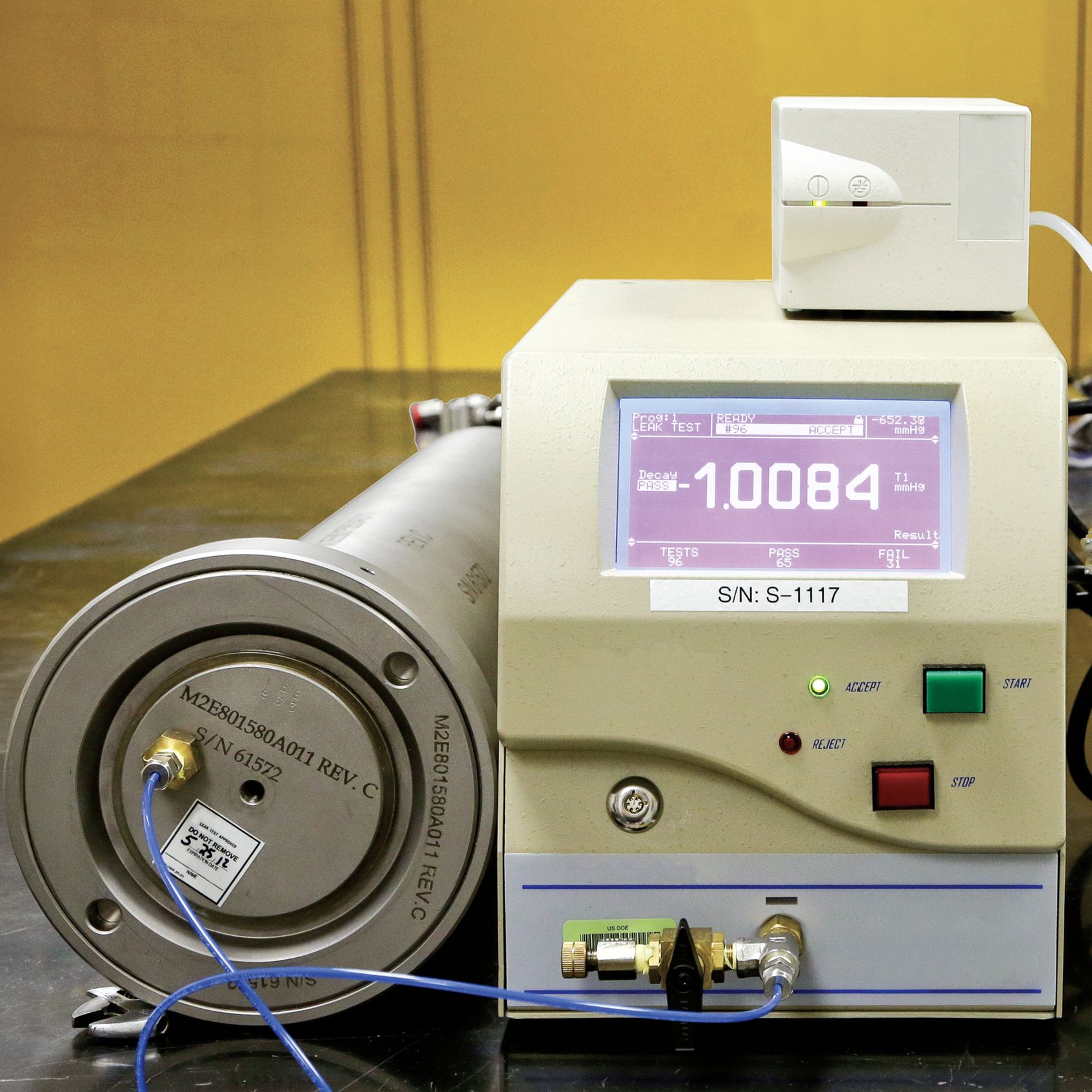 A machine with a digital display reading "1.0084" connected to a cylindrical component with wires.