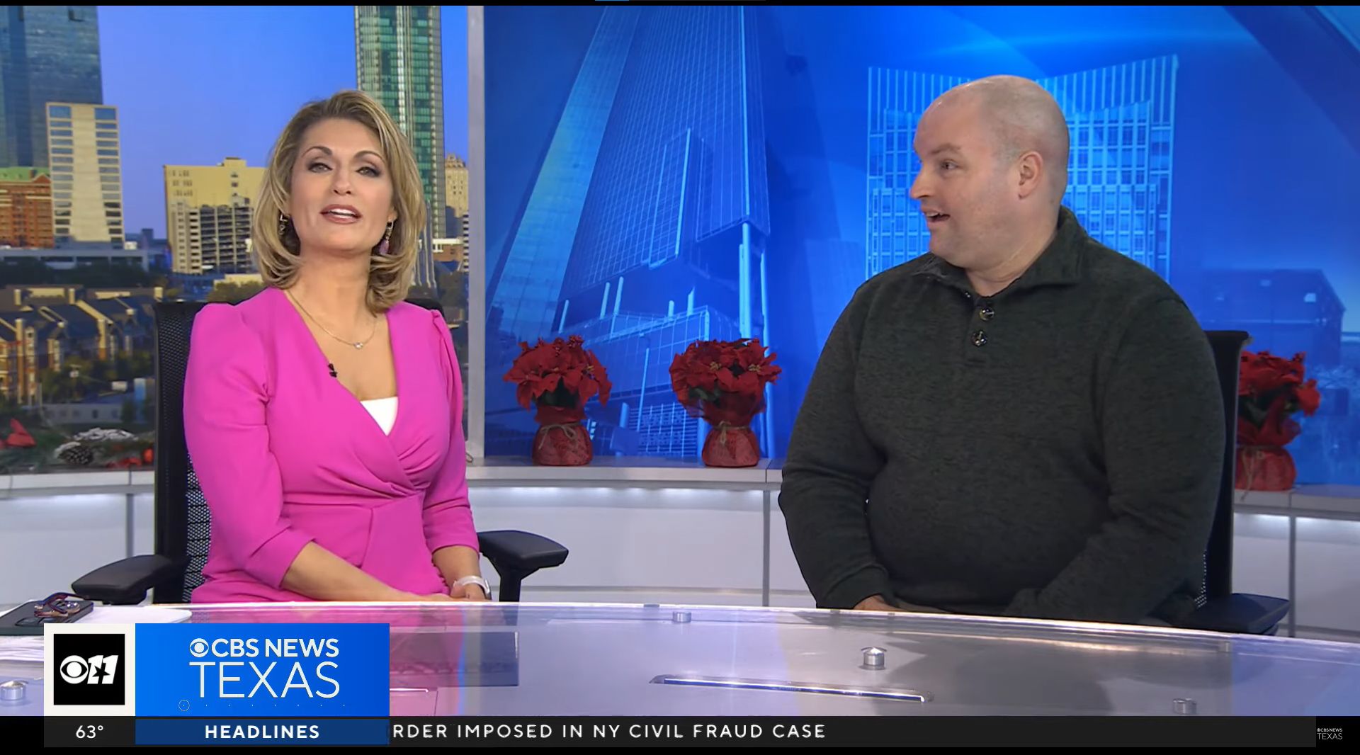 A CBS News Texas anchor in a pink outfit sitting next to Jared Watson in a dark green sweater during a broadcast, with the city skyline in the background.
