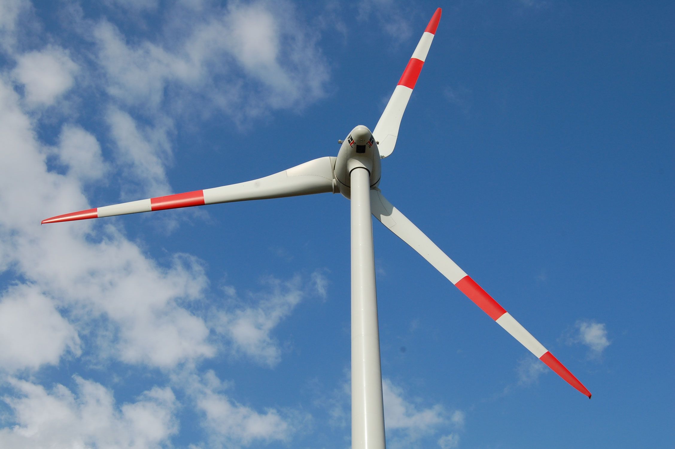 Wind turbine with red-tipped white blades against a blue sky with scattered clouds