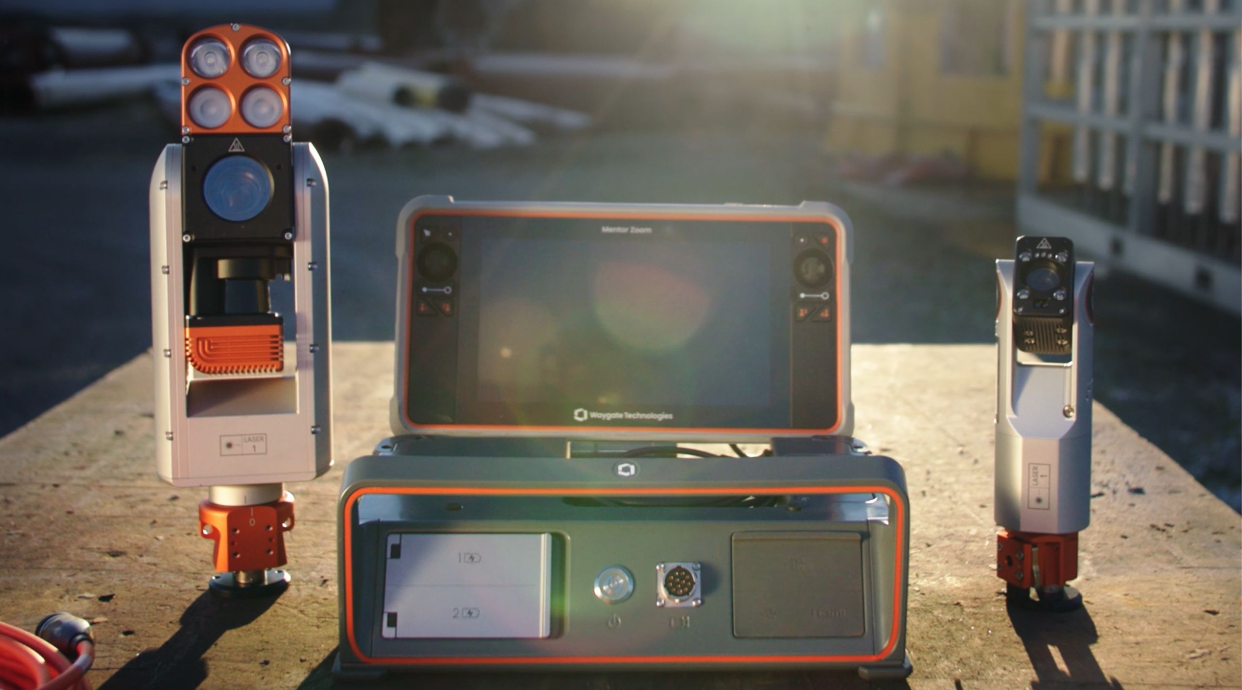 Two modes of the Waygate Mentor Zoom displayed outdoors, including a central touchscreen device, illuminated by sunlight.