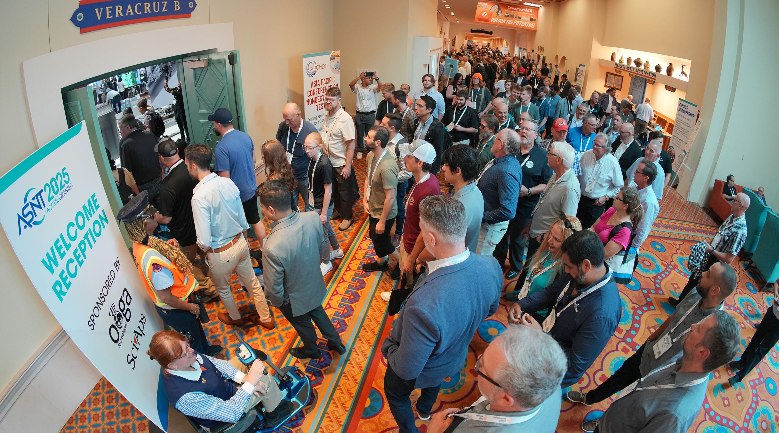 A large crowd gathers at a conference entrance, with a sign for the 2025 ASNT Welcome Reception visible.