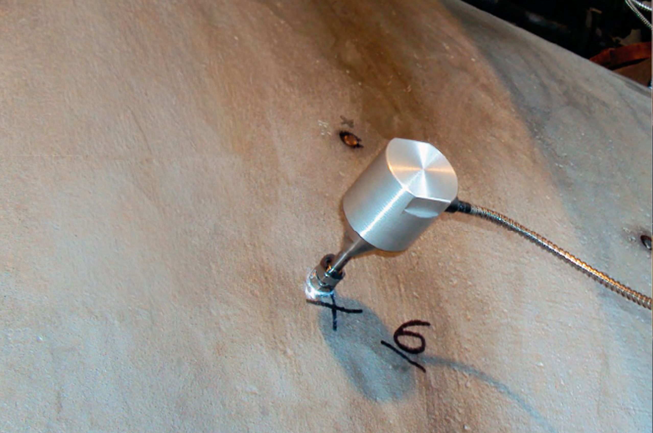 Metal sensor on a concrete surface, with markings "X" and "6" near the sensor contact point.