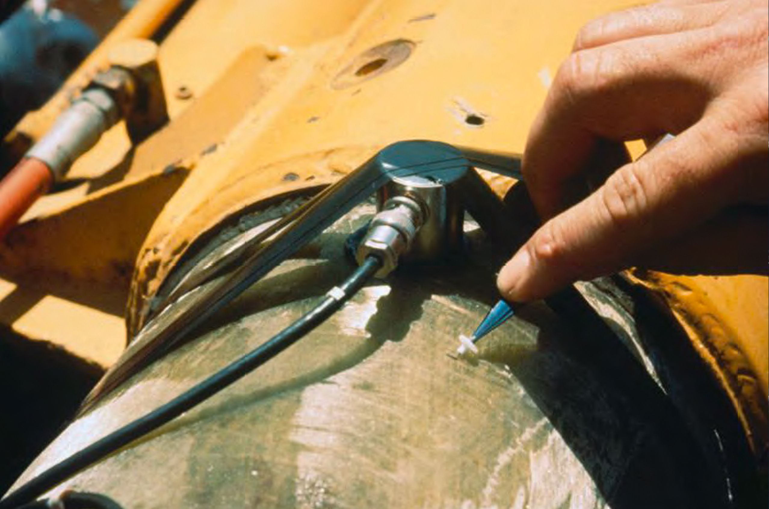 Hand places a small component near a sensor on a metal surface, mounted on a yellow mechanical structure.